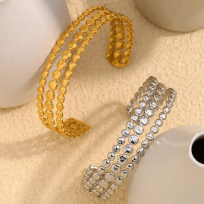 A lifestyle shot of the Aria cuff bracelets in both gold and silver finishes nestled between white ceramic objects.