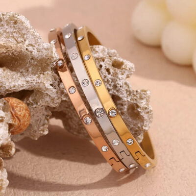 A close-up of three Aura zirconia bangles on coral, highlighting the secure hinged clasp on the 18k gold plated bangle.