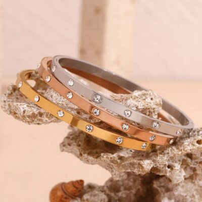 The three Aura zirconia bangles in gold, rose gold, and silver artistically arranged on a piece of natural white coral.