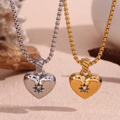 The celestial heart necklaces shown side-by-side in both 18k gold and polished silver finishes on a textured surface.