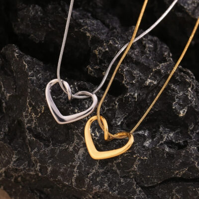 Close-up of the 18k gold and silver entwined heart necklaces displayed on a dark, textured rock.