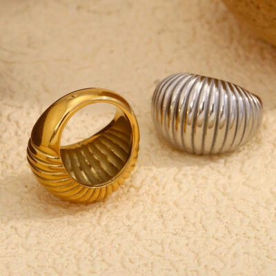 The 18k gold croissant ring turned to show its interior, resting next to the silver version on a textured surface.