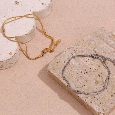 The gold and silver double strand knot bracelets arranged on a stone block, showing their minimalist aesthetic.