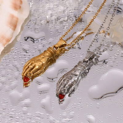 The gold and silver hand necklaces resting on a wet, reflective surface with water droplets, demonstrating their waterproof quality.